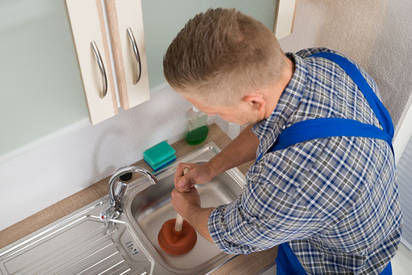 A plumber with a plunger unblocking a sink.