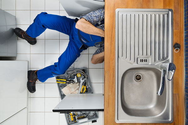 A plumber checking the pipes under a kitchen sink.